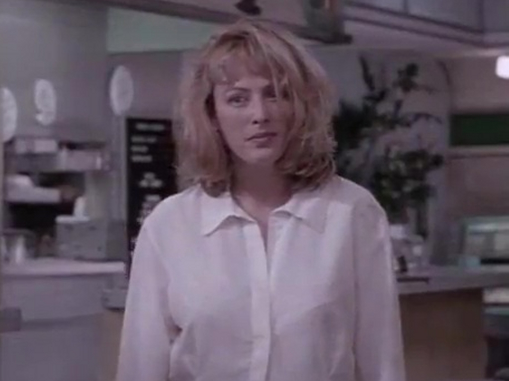 Virginia Madsen as Kim in Just Your Luck, standing in a diner wearing a white shirt, looking thoughtful with slightly tousled hair.